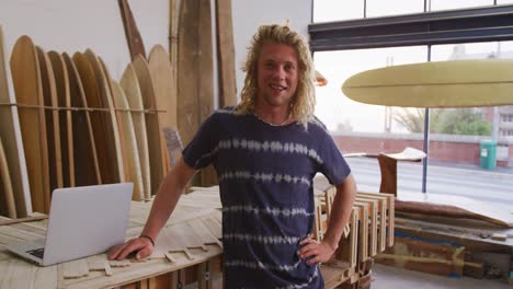 caucasian male surfboard maker in his studio with surfboards in background