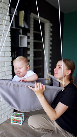 woman holds a swing with her child sitting inside. mother and son at home having fun time. vertical video.