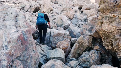 female hiker with blue backpack hikes up boulder field