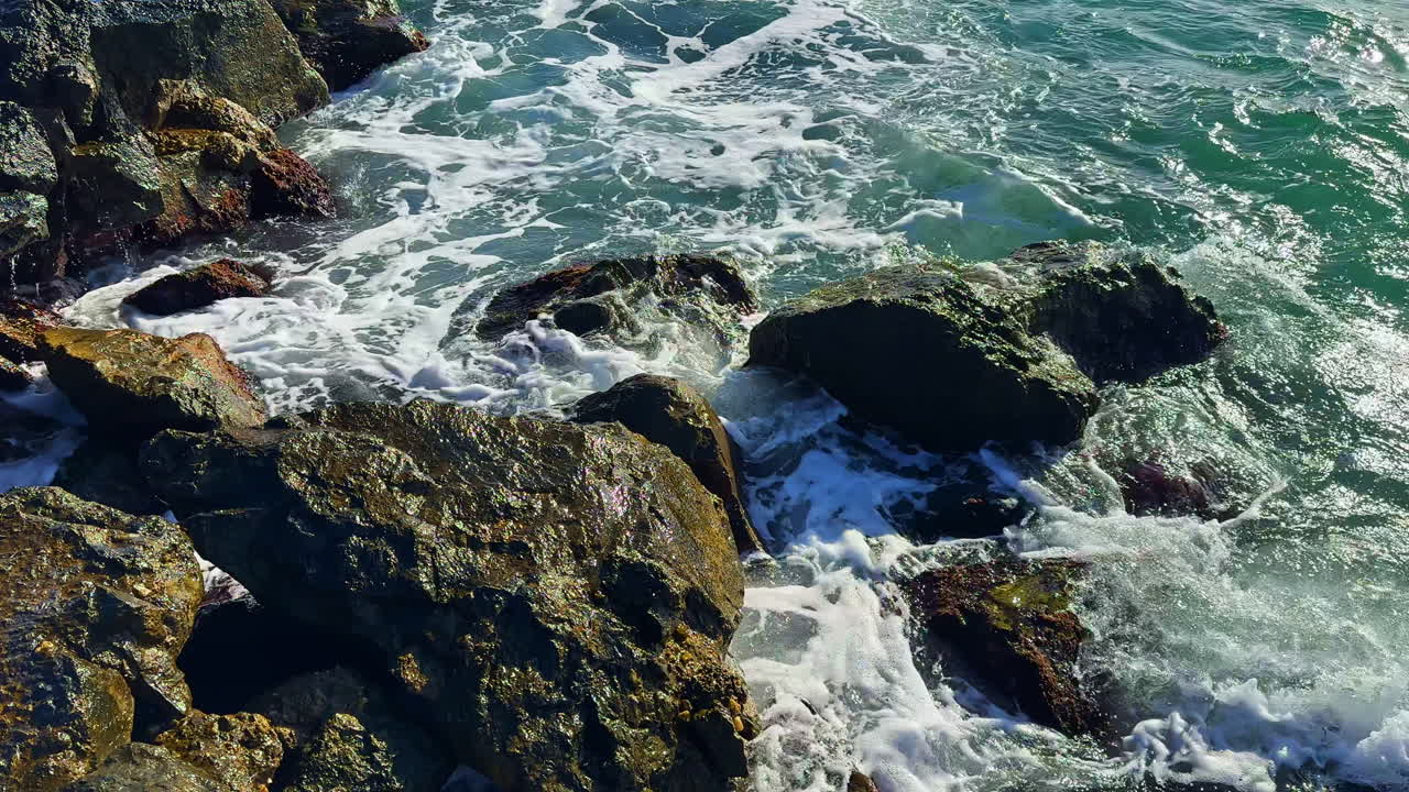 Le onde si infrangono sugli scogli vicino alla riva durante il giorno, creando spruzzi e schiuma in un paesaggio oceanico.