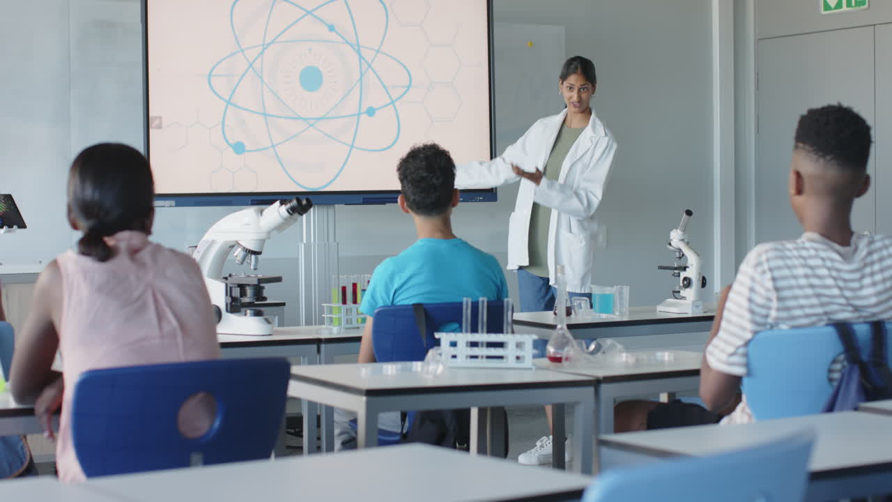 Teaching science, instructor in lab coat presenting to students in school classroom
