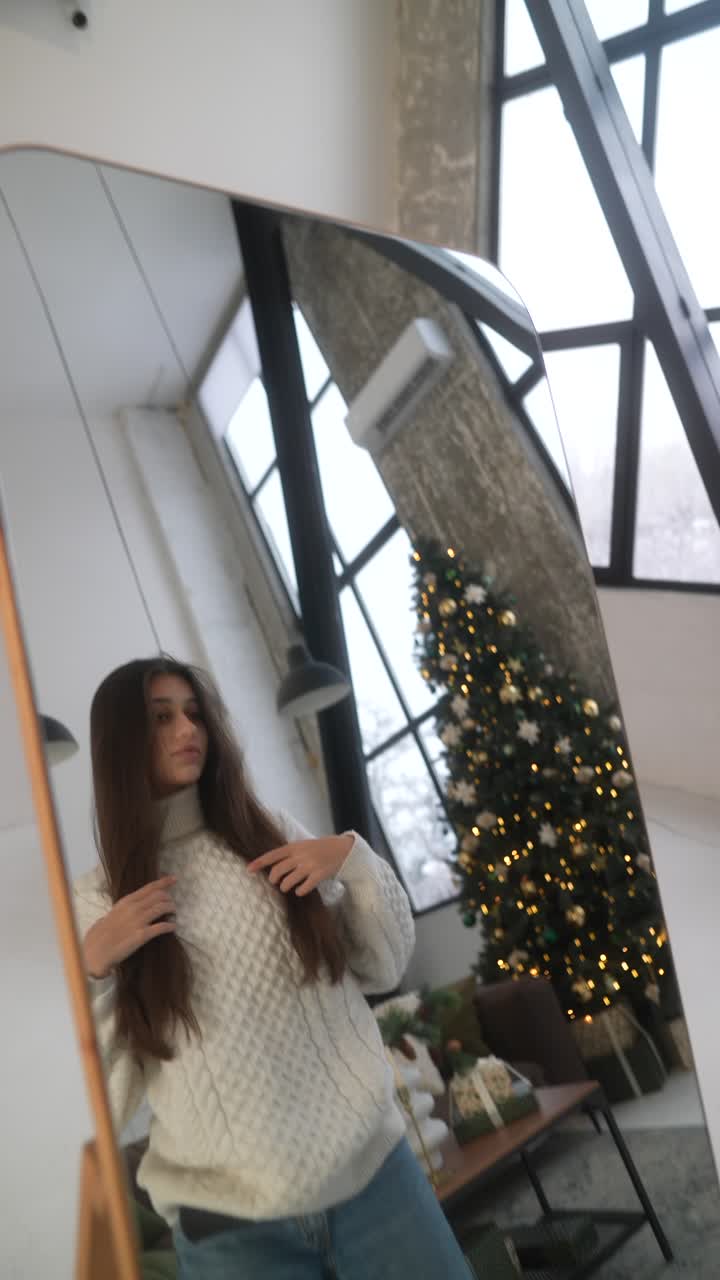 Donna con un maglione che si guarda allo specchio vicino a un albero di Natale
