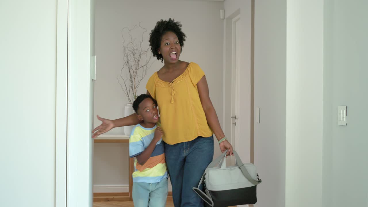 African American mother and son entering home, front door opening, mother carrying bag, reuniting