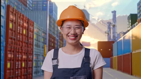 close up of asian woman worker wearing goggles and safety helmet standing and smiling to camera at container yard warehouse