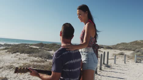 feliz pareja caucásica sentada en la playa junto al mar tocando la guitarra