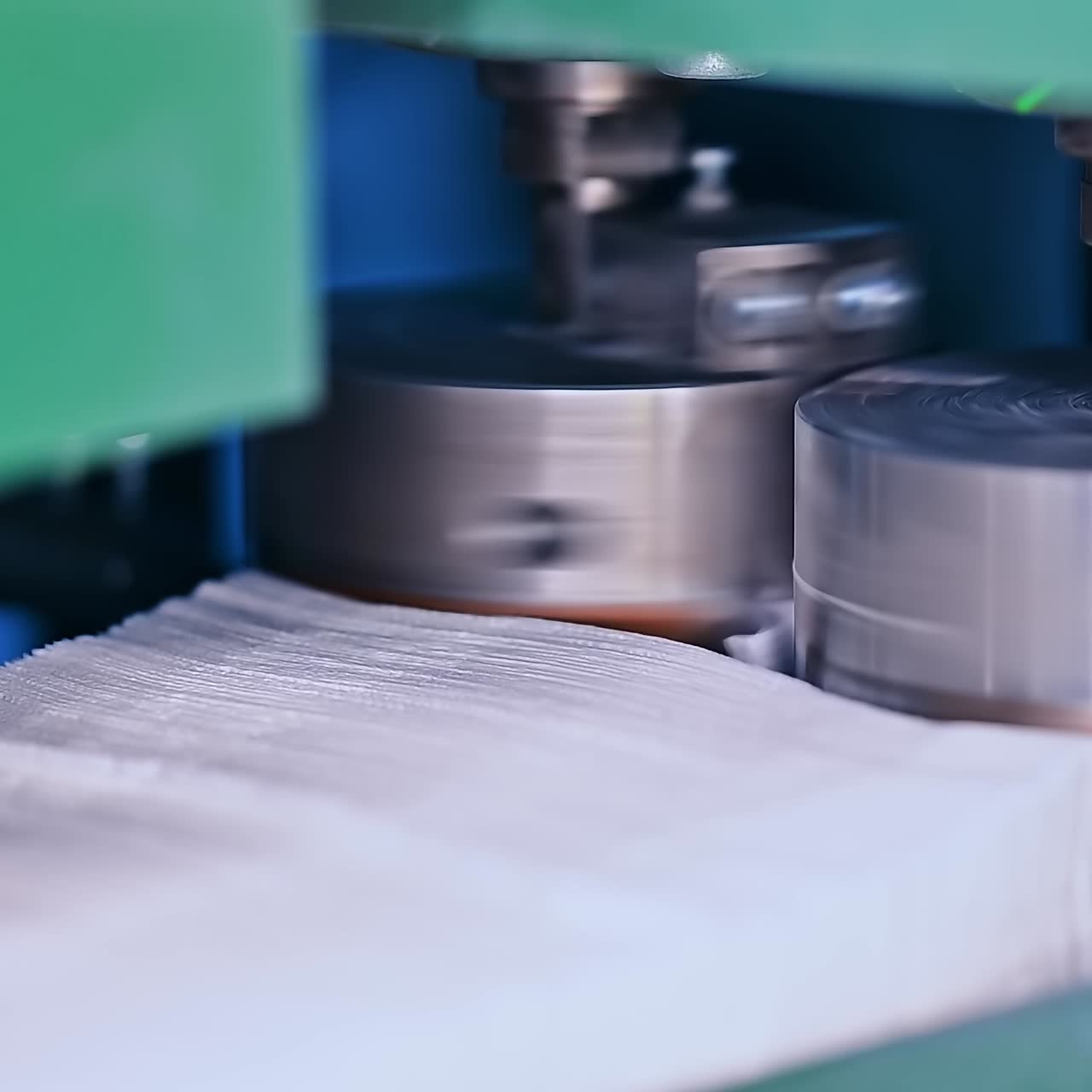 Thick spinning metal shafts pushing the fabrics for future diapers. Stack of non-woven cloths for nappies. Close up