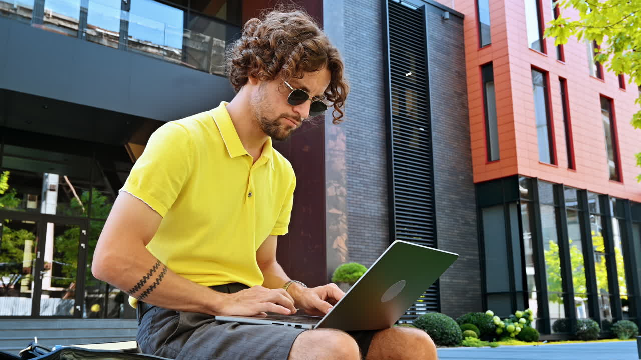 Man in yellow shirt talking standing on a bench and working on a laptop
