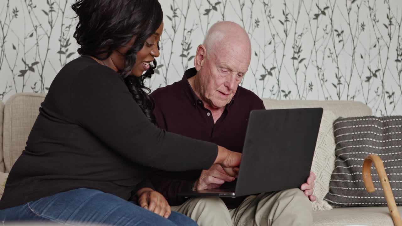 Caregiver assisting senior man with laptop