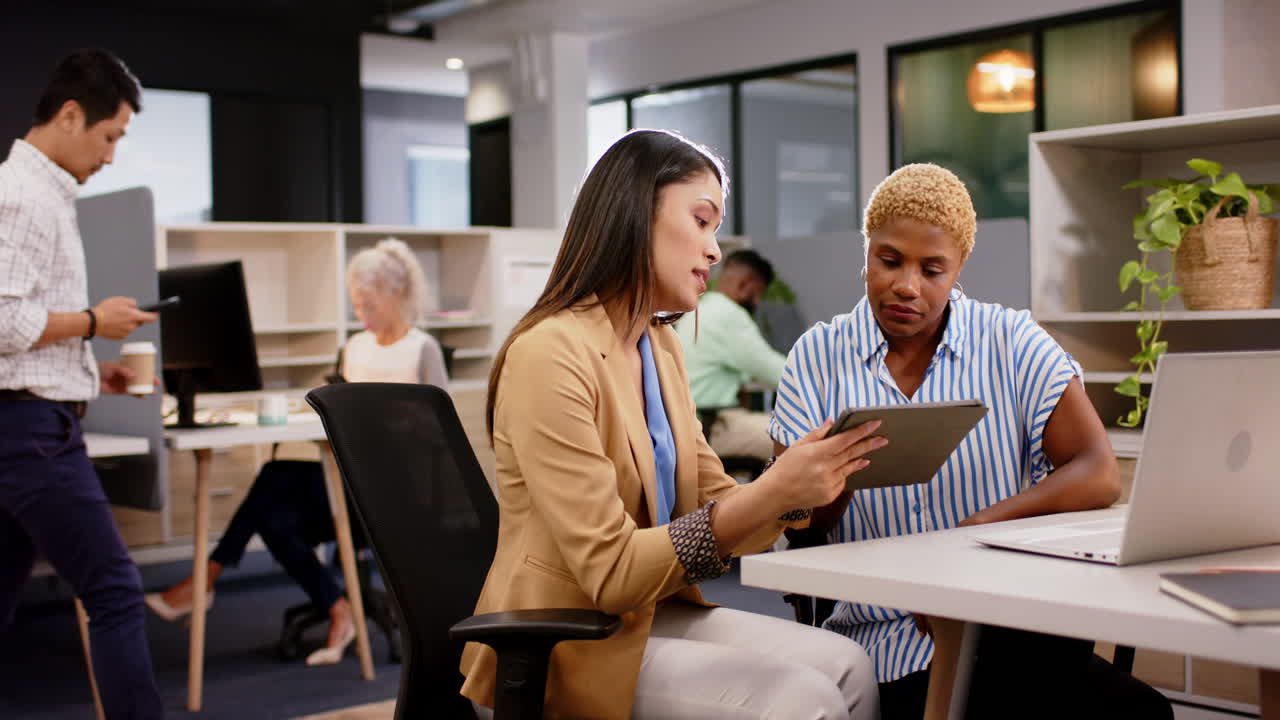 Discussing project details, businesswomen using tablet in modern office workspace