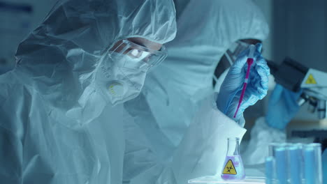 female chemist in protective uniform dripping reagent into flask with liquid
