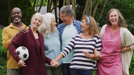 animation of happy diverse female and male senior friends in garden, holding ball, posing to photo