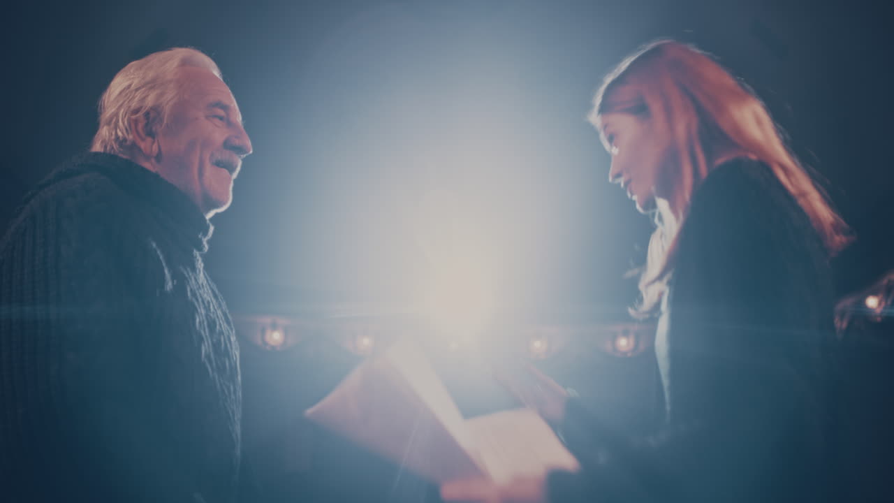 Senior Director Teaching Actress to do Quarrel Scene Pan Left View of Elderly Man Teaching Young Woman with Script to do Argument Scene during Rehearsal on Stage in Theater