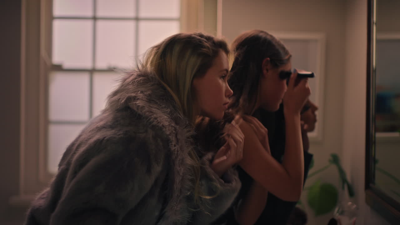 행복한 여자 친구들이 준비하고 거울을 보며 메이크업하는 십대들이 스타일리쉬한 패션을 입고 나갈 준비를 하고 있습니다.