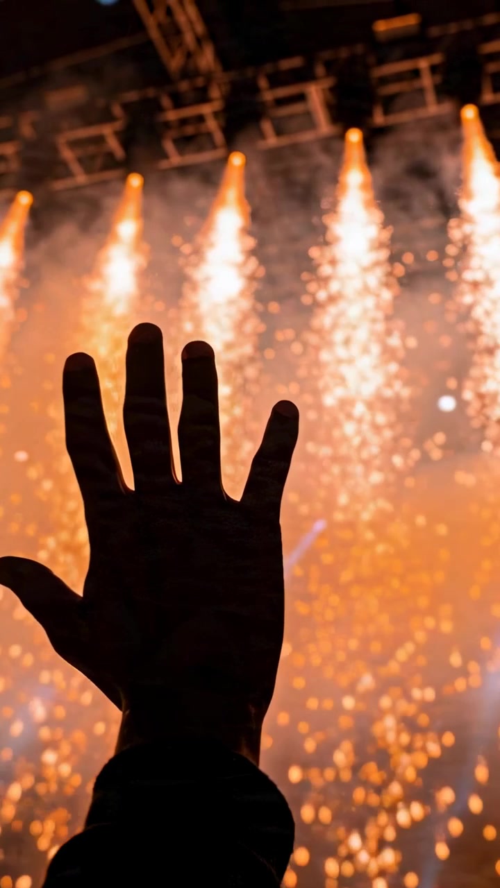 Video vertikal: Tangan gelap mengangkat di puncak konser dengan manset dan gelang saat air mancur menyala
