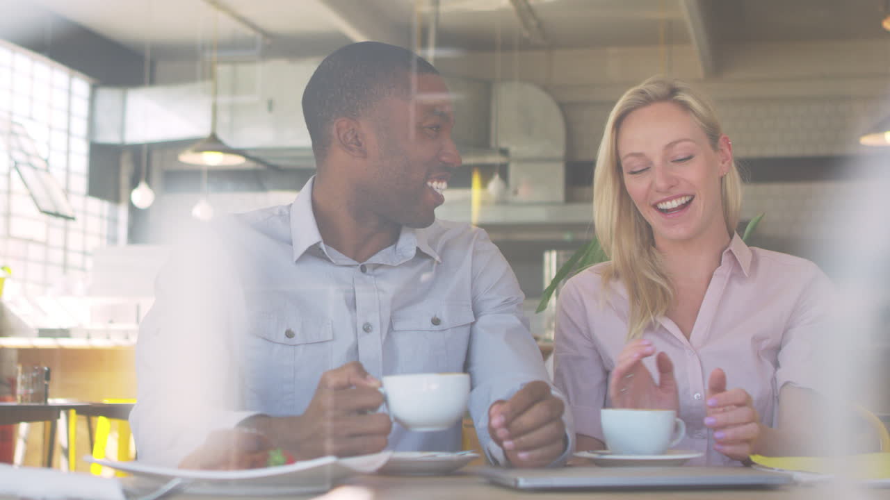 una pareja se reúne para una cita en una cafetería disparada a través de la ventana.