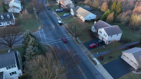 aerial tracking shot of red car driving through american suburb in winter