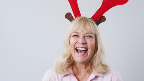 Studio-Shot-Of-Happy-Mature-Woman-Wearing-Dressing-Up-Reindeer-Antlers-Against-White-Background