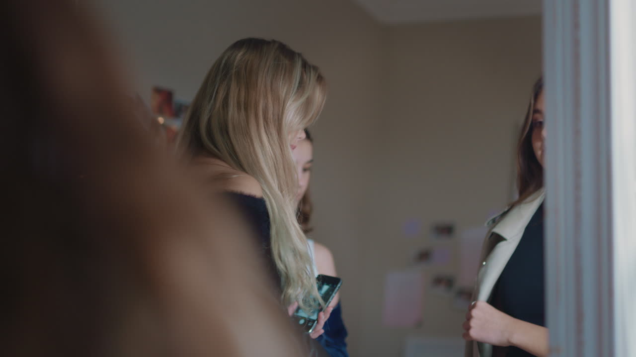 행복한 여자 친구들이 스마트폰을 사용하여 셀카 사진을 찍고 거울에 포즈를 취하고 소셜 미디어에서 세련된 패션을 공유하고 주말을 집에서 즐기며 함께 어울립니다.