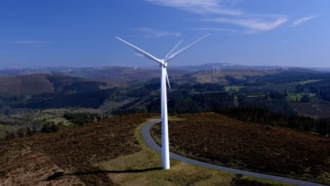 Zwei-Windturbinen-Drehten-Ihre-Blätter-In-Den-Bergen-Mit-Kleinen-Grünen-Baumwäldern-An-Einem-Sonnigen-Nachmittag-Mit-Blauem-Himmel