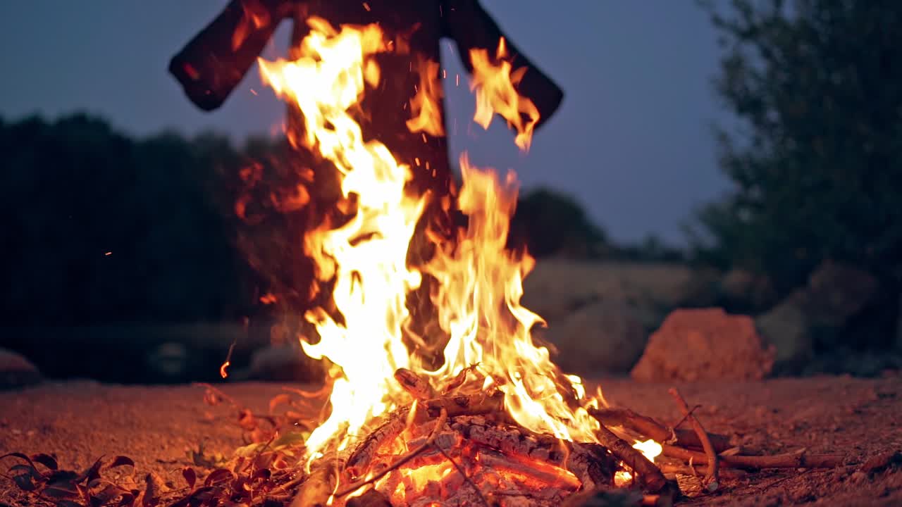 Bright campfire and black costume without hands behind. Fire and witch in nature in the evening. Slow motion.