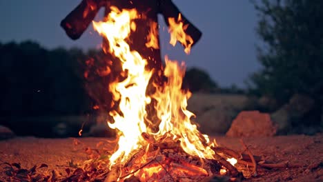 bright campfire and black costume without hands behind. fire and witch in nature in the evening. slow motion.