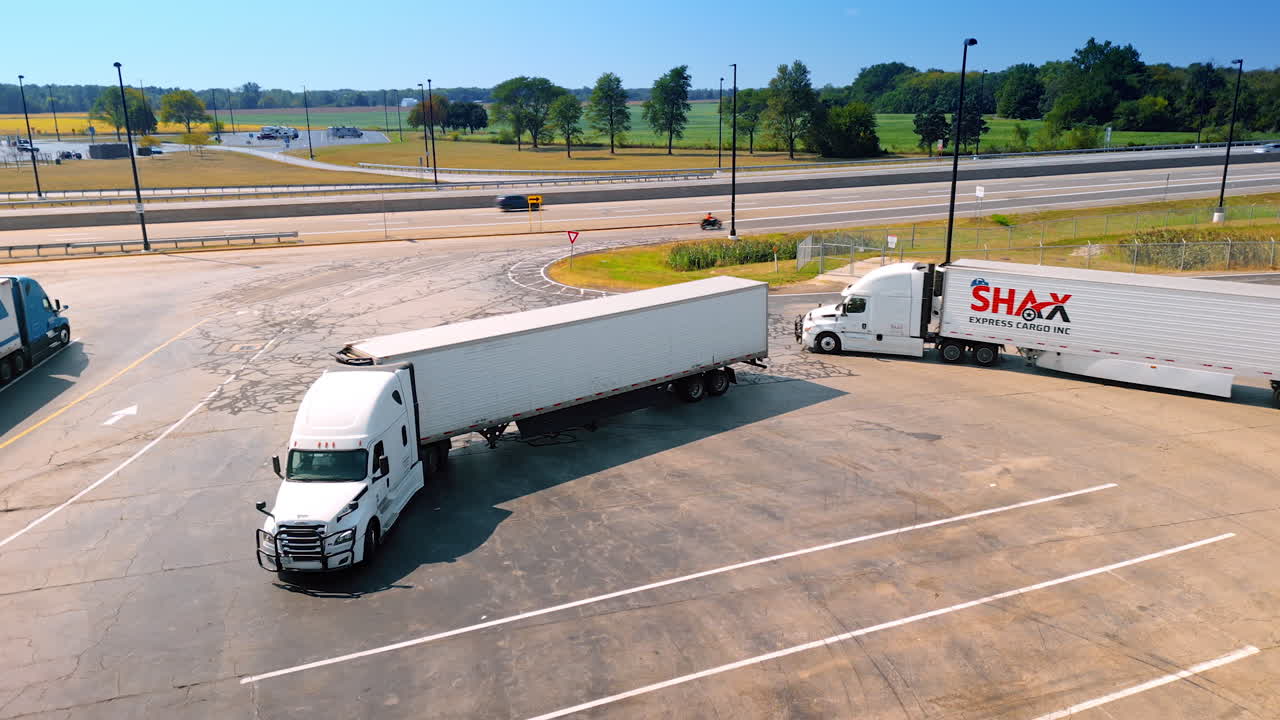 Chicago, USA, 29 June 2025: Drone shot of freight trucks turning and parking at a logistics rest area along the highway with fields in the background