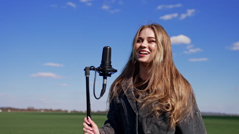 beautiful singer on blue sky background. young woman singing and jumping near the microphone while performing concert outdoors.