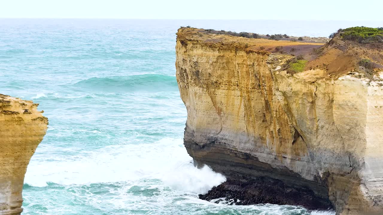 Dynamic ocean waves crash against rugged cliffs under bright daylight at Port Campbell, creating a dramatic coastal scene