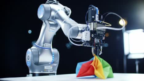 a robotic arm skillfully manipulates colorful origami creations, showcasing precision in automated craftsmanship and innovative design under studio lights