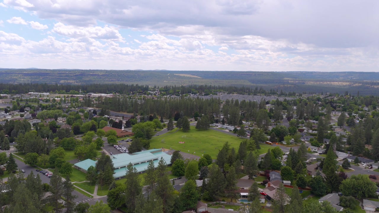 Vista aérea de un barrio de Spokane, WA con una piscina comunitaria, un campo de parque abierto y calles arboladas bajo un cielo nublado