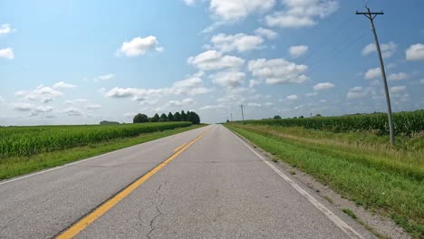 pov - driving on a rural county road towards a rural home and past fertile fields in late summer in central iowa