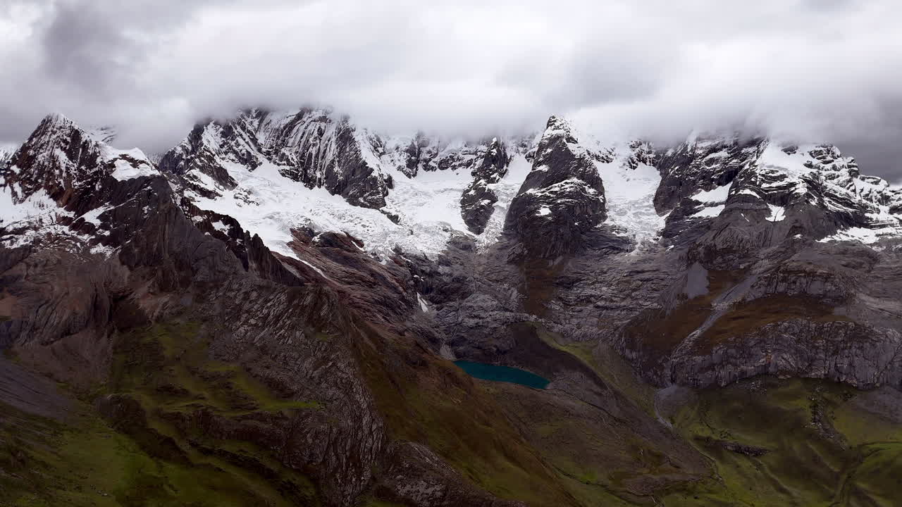 Cinematic aerial view of snowy Andes mountains in Peru with glaciers, rocky cliffs, and hidden blue alpine lake under misty clouds, dramatic landscape and natural travel destination