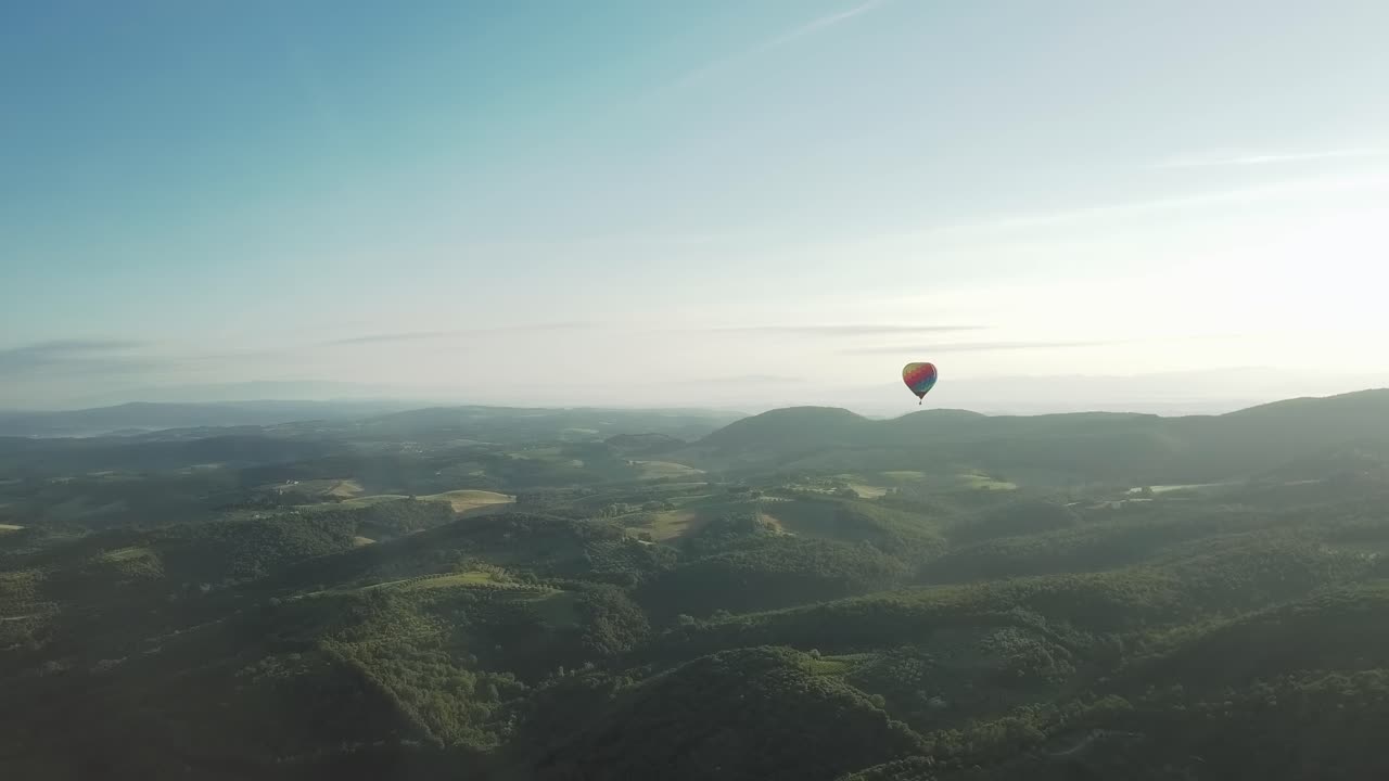 disparo de un dron de un colorido globo aerostático al amanecer sobre las ondulantes colinas toscanas