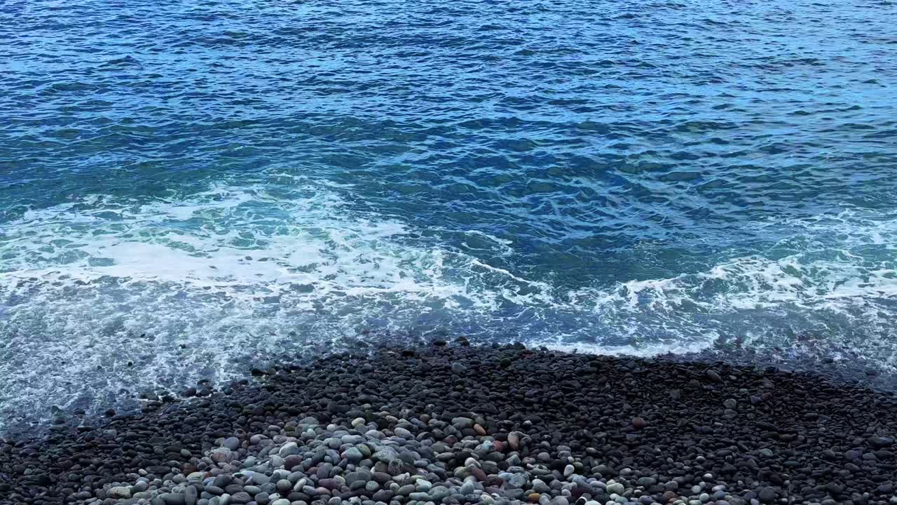 el agua del océano azul limpio se lava en la playa de piedras de guijarros en tenerife, españa