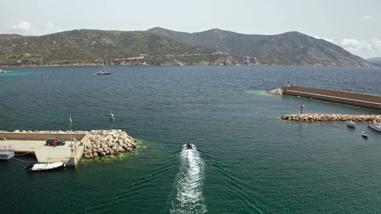 A speedboat leaving a harbor with mountains in the background in Sardinia on a sunny day