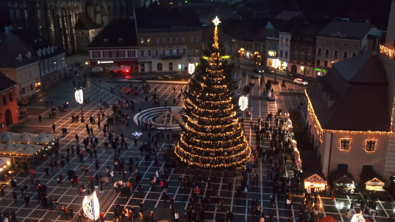 Aerial drone view of The Council Square at dusk in Brasov, Romania. Old city centre decorated for Christmas. County Museum of History, buildings, people