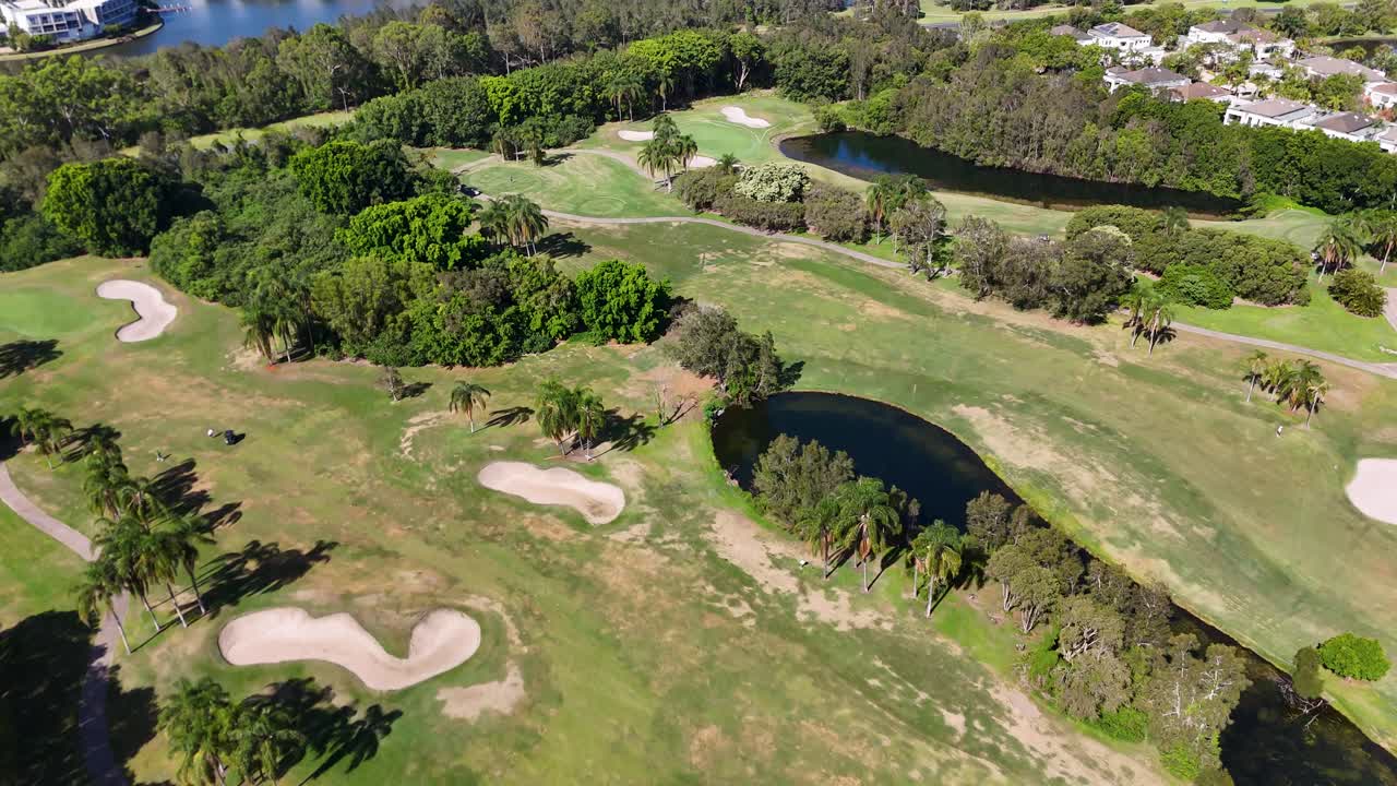 Sunny daytime drone flyover of lush golf course fairway, sand bunkers, lakes, and trees
