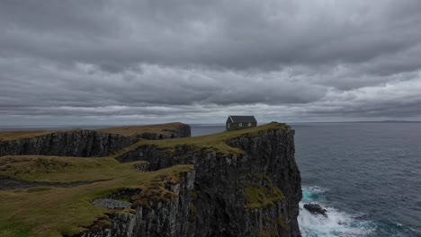 lone house sits atop a rugged cliff overlooking a turbulent sea under a moody, overcast sky. the scene captures the essence of isolation and the raw power of nature