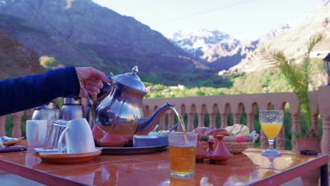 Sirviendo-Té-De-Una-Tetera-Plateada-En-La-Terraza-De-La-Azotea,-Marruecos,-Cámara-Lenta