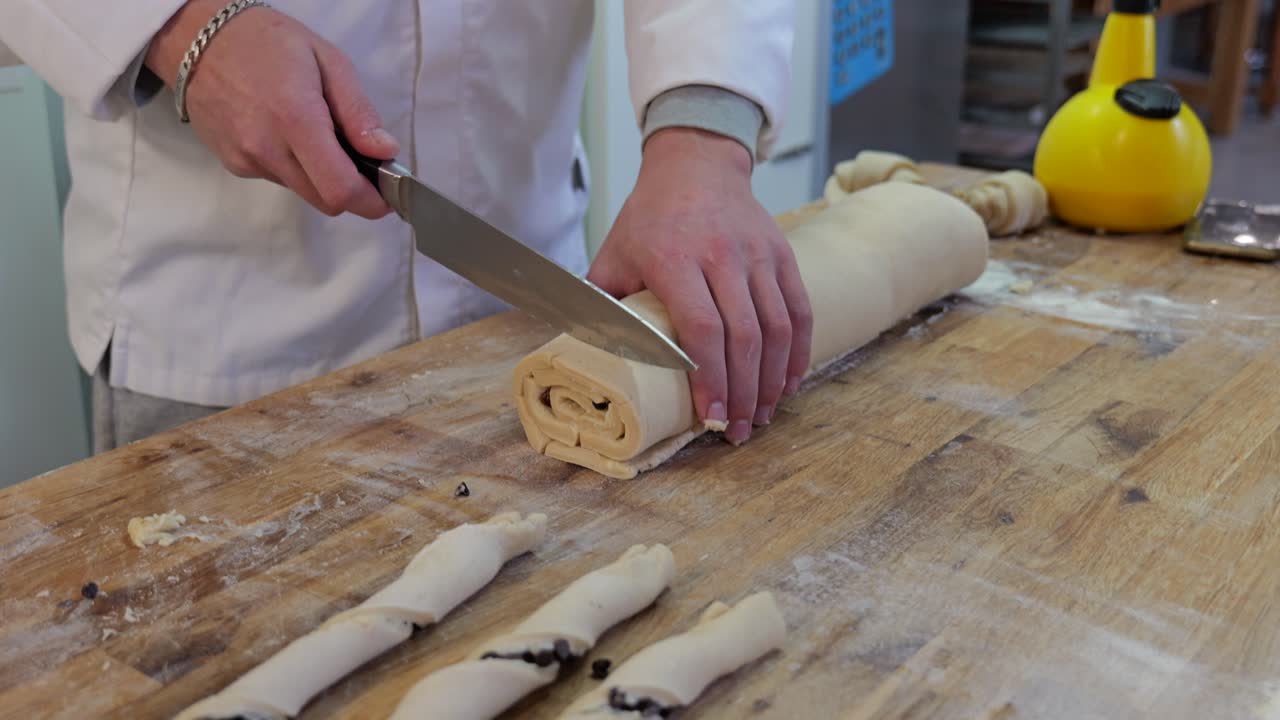 Primo piano di un panettiere che taglia a fette un impasto arrotolato con gocce di cioccolato all'interno.