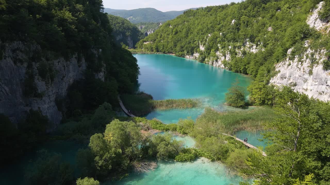 vista superior del hermoso parque nacional de los lagos de plitvice con muchas plantas verdes y hermosos lagos y cascadas, así como el camino hacia el desfiladero por el que va la gente