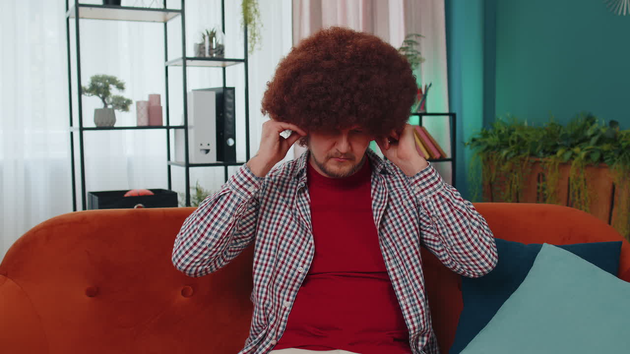 Happy relaxed guy in wireless headphones dancing listening favorite rock n roll music on home couch