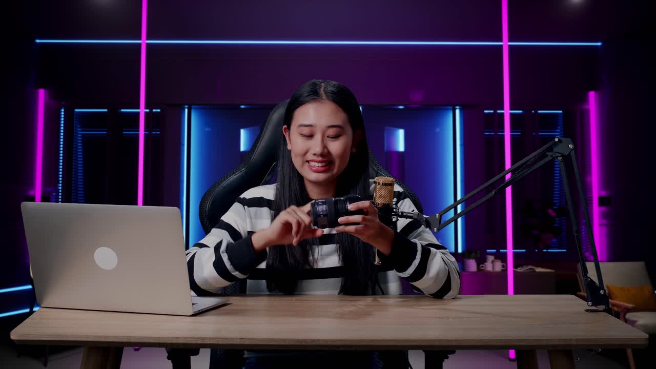 una mujer asiática sonriente con computadora revisando la cámara len en la habitación iluminada por luces de neón en retro