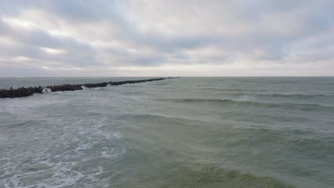 establecimiento de una vista aérea de un hombre dedicado al kitesurf, día de invierno nublado, olas altas, deporte extremo, playa de karosta del mar báltico, muelle de piedra a la izquierda, tiro de drones avanzando