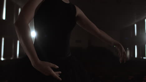 prima ballet company in a dark dress on a dark theater stage rehearsing in the smoke performs dance moves in slow motion.