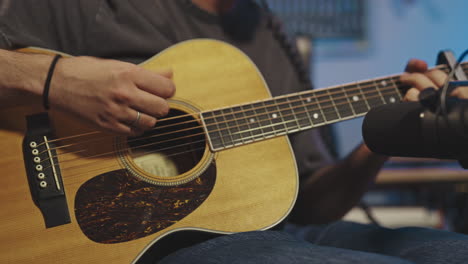 skilled caucasian professional musician recording acoustic guitar in studio with microphone