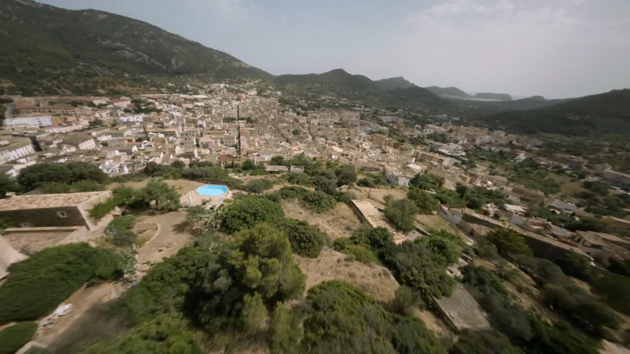 FPV Aerial drone shot over old town of Andratx surrounded by mountain range in Mallorca, Spain on a bright sunny day