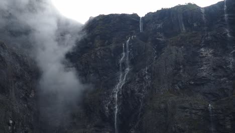 Dark-rocky-cliffs-with-mis-and-waterfalls-falling-into-the-depths