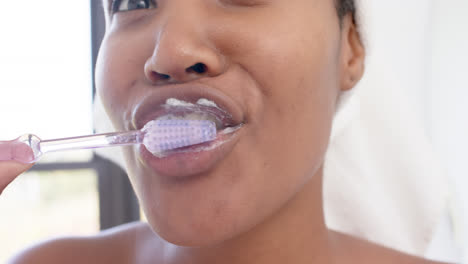 Portrait-of-happy-biracial-woman-with-towel-on-head-brushing-teeth,-slow-motion