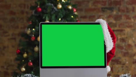 sombrero de santa colgado en el monitor de la computadora con espacio de copia, con decoraciones de navidad y árbol